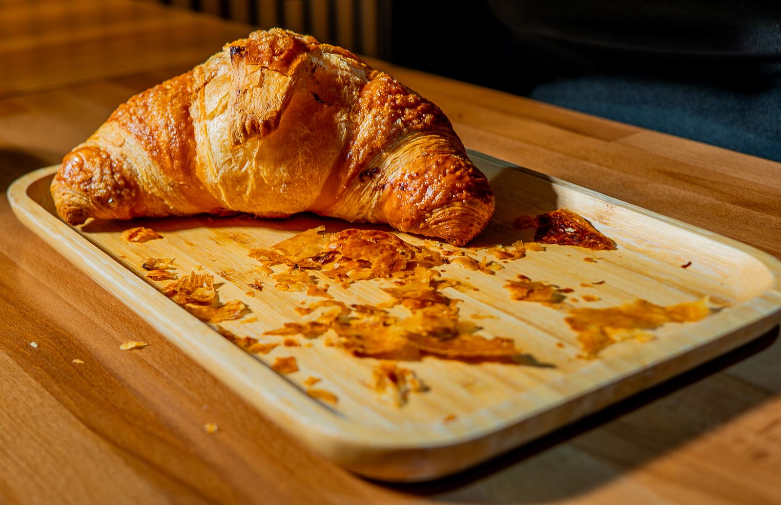 Croissant on a wooden tray with flaky crumbs at a NYC café