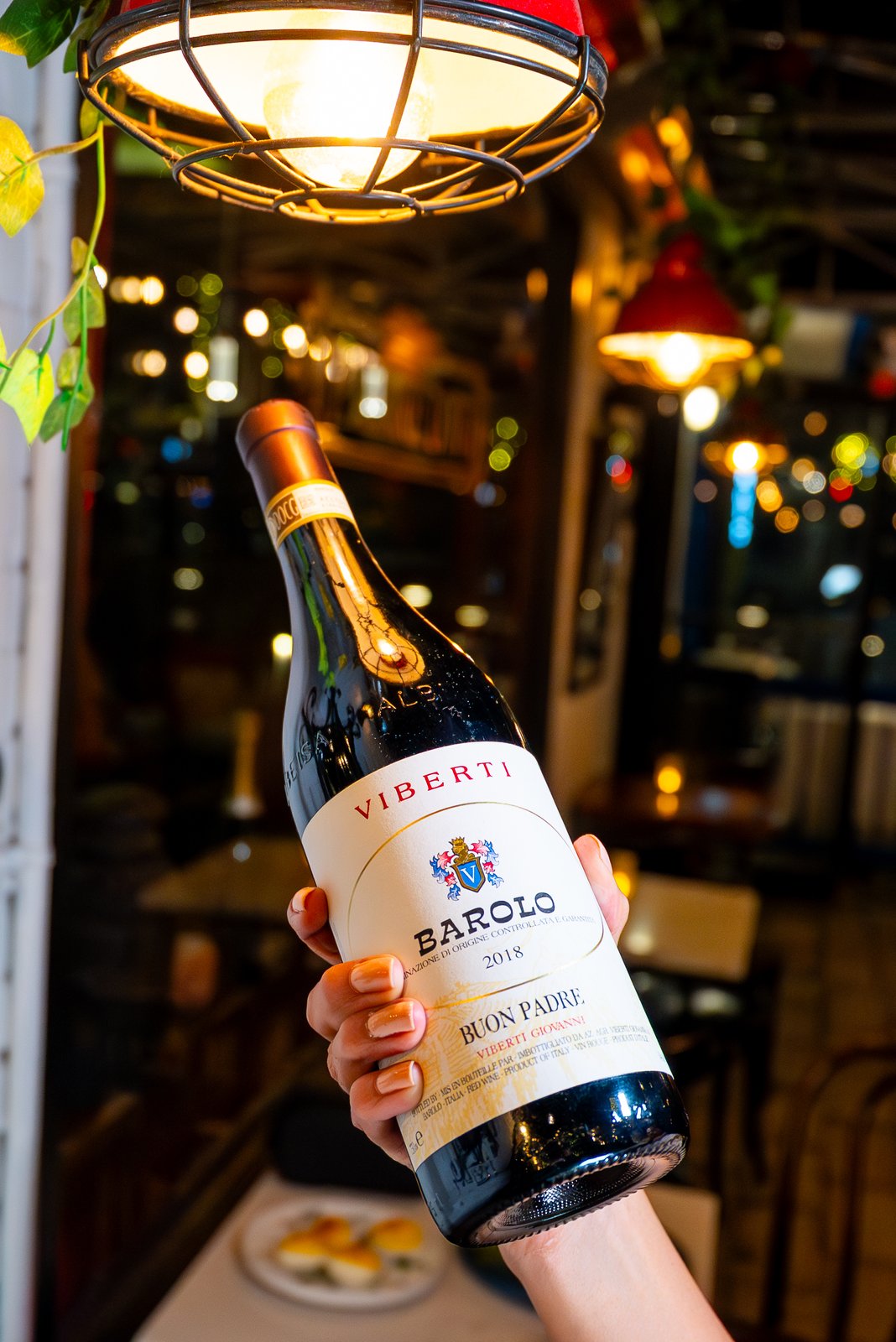 Bottle of Barolo held under a pendant light at a NYC wine bar, shot for a Getalife Studios client